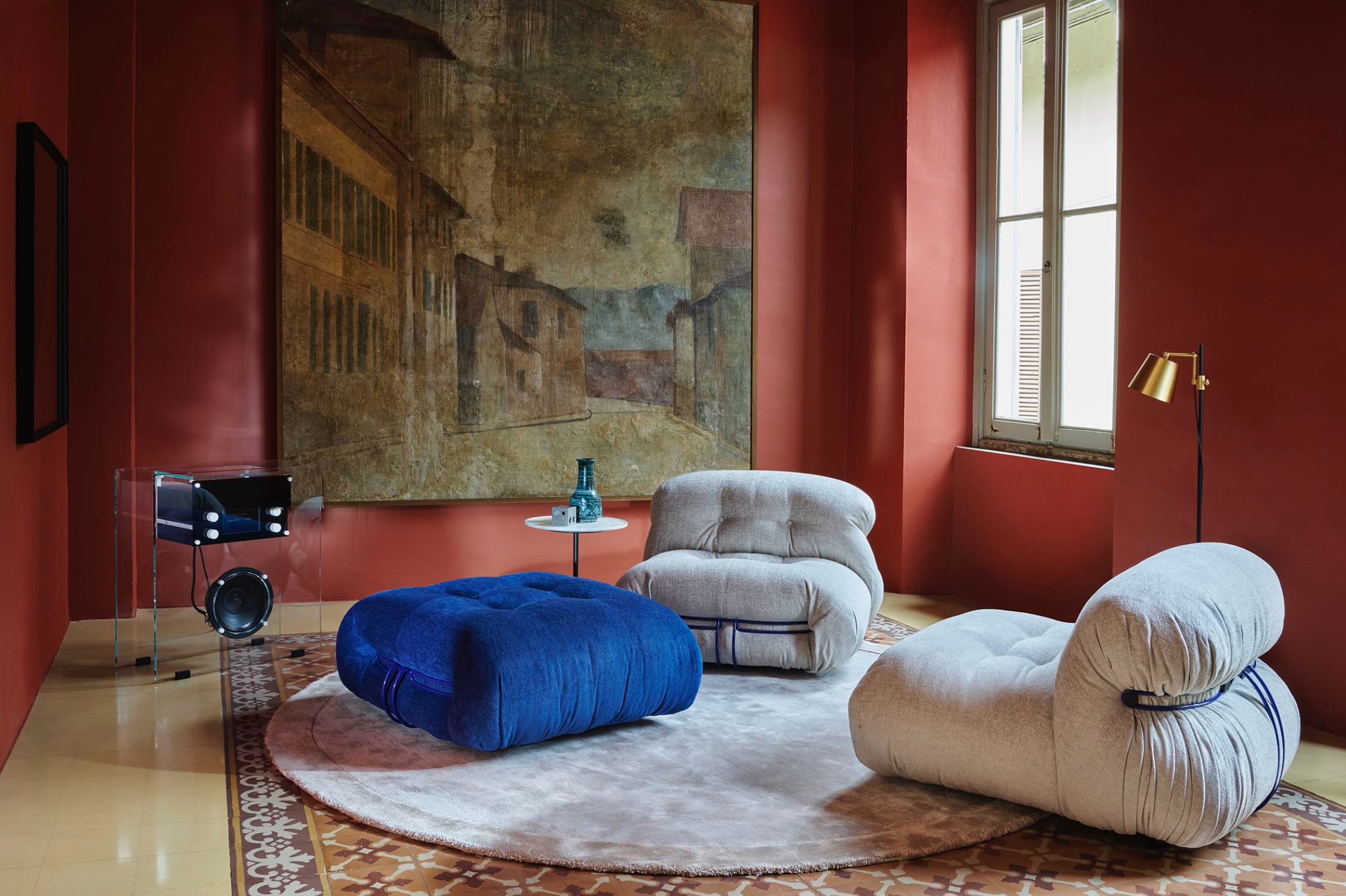 An interior with upholstered chairs, a blue ottoman and a large artwork.